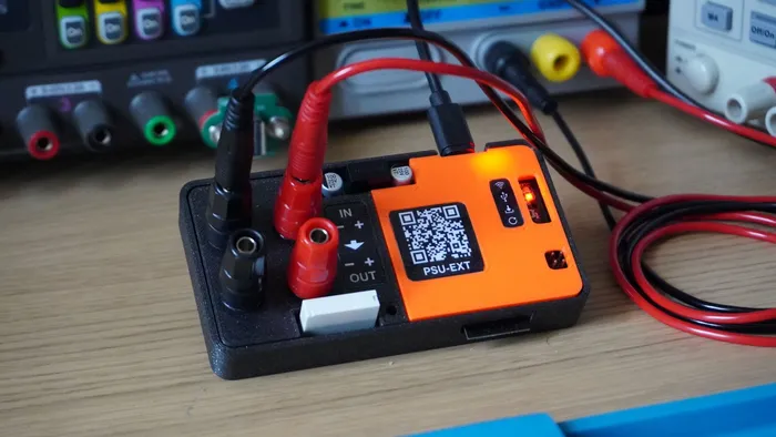 PSU-EXT in its enclosure on a bench, wired to a bench PSU and connected via USB-C, with Wi-Fi and USB status indicators lit